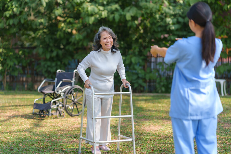 Brain & Spinal Cord Injuries Need Specialized Proven Rehabilitation - Asian woman with walker steping toward fmale therapist on grass outside
