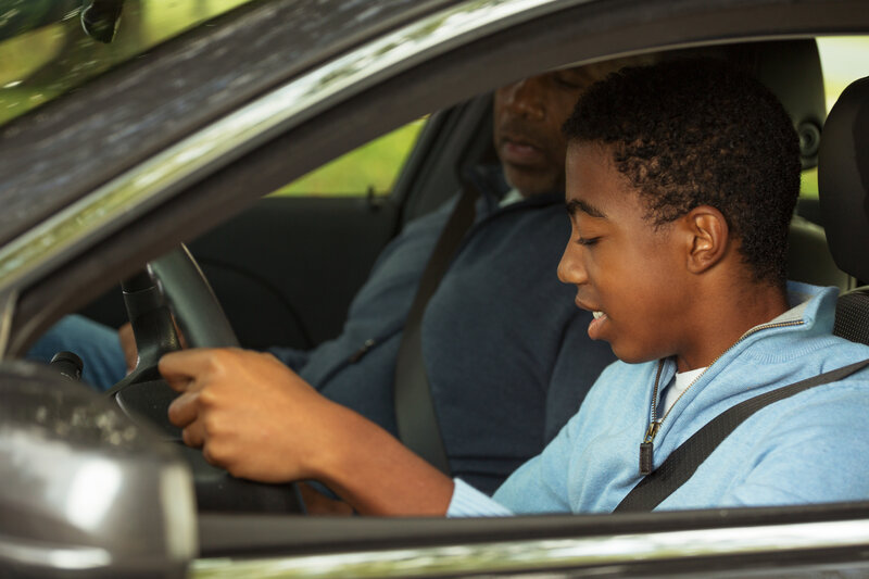 African American father and son in the front seat of a car having a driving lesson. brain injury recovery