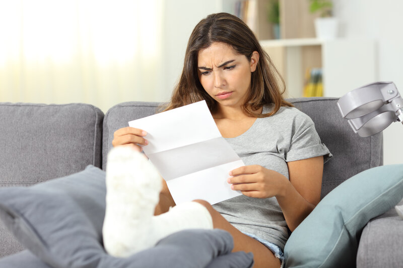 Girl with leg in cast and crutches siting on couch looking worriedly at a peice of paper. Case management