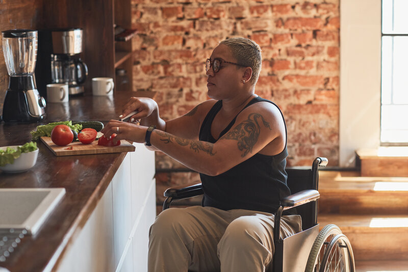 Side view portrait of contemporary tattooed woman with disability cooking dinner at home, copy space - chronic condition