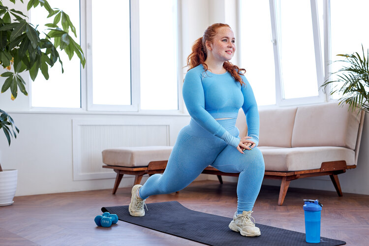 Obesity & Metabolic Health After Brain Injury - redheaded youn female doing yoga in blue clothes overweight freckled woman doing stretching exercise at home, on fitness mat. attractive caucasian lady in blue sportswear is engaged in sport, preparing for yoga, workout training in living room