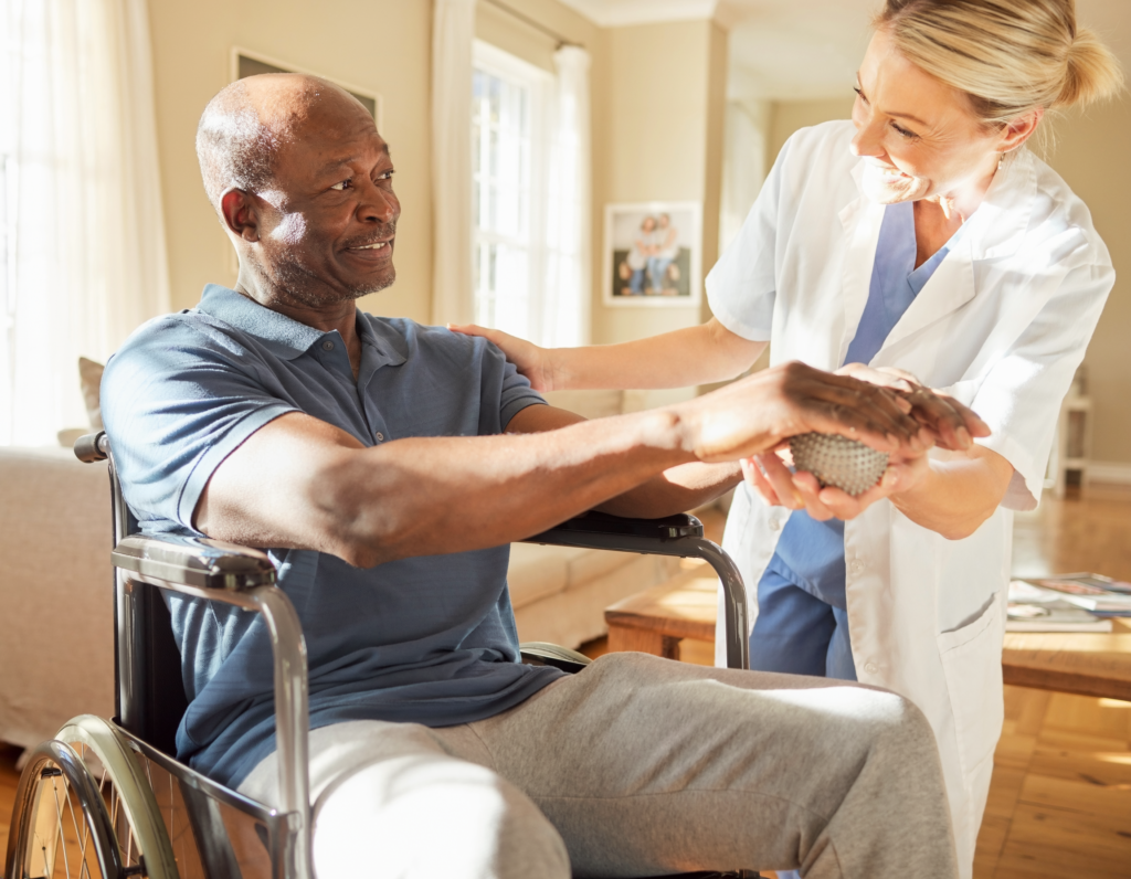 Brain Injury Basics - Adult African American male in a wheel chair doing hand exercises with a ball and the help of a blonde middle aged female theraapist.