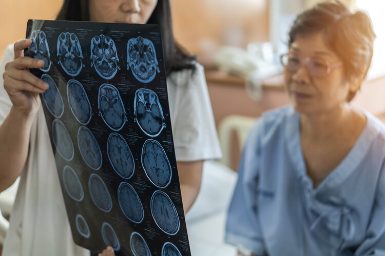 Brain Injury Basics - Female doctor holding up brain scans for mature Asian female patient to look at.