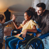 Happy multiethnic loving family. Smiling little girl with disability in wheelchair at home. When Coverage Changes: How To Provide Stable Home Rehab